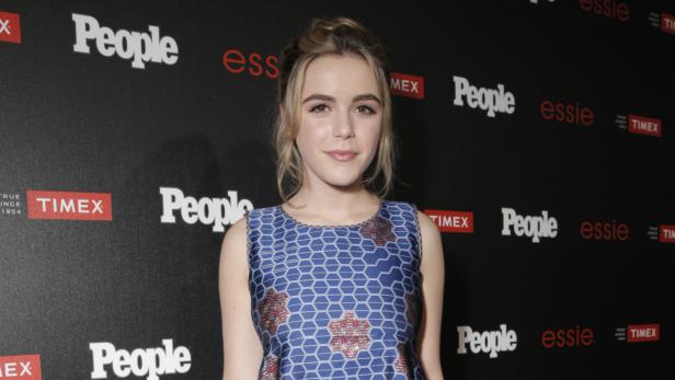 Kiernan Shipka posiert vor einer Wand mit Logos von People, Essie und Timex.