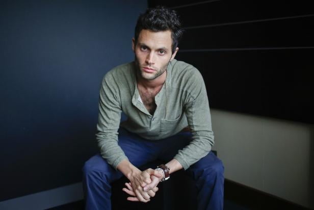Penn Badgley sitzt vor einer dunklen Wand und blickt in die Kamera.
