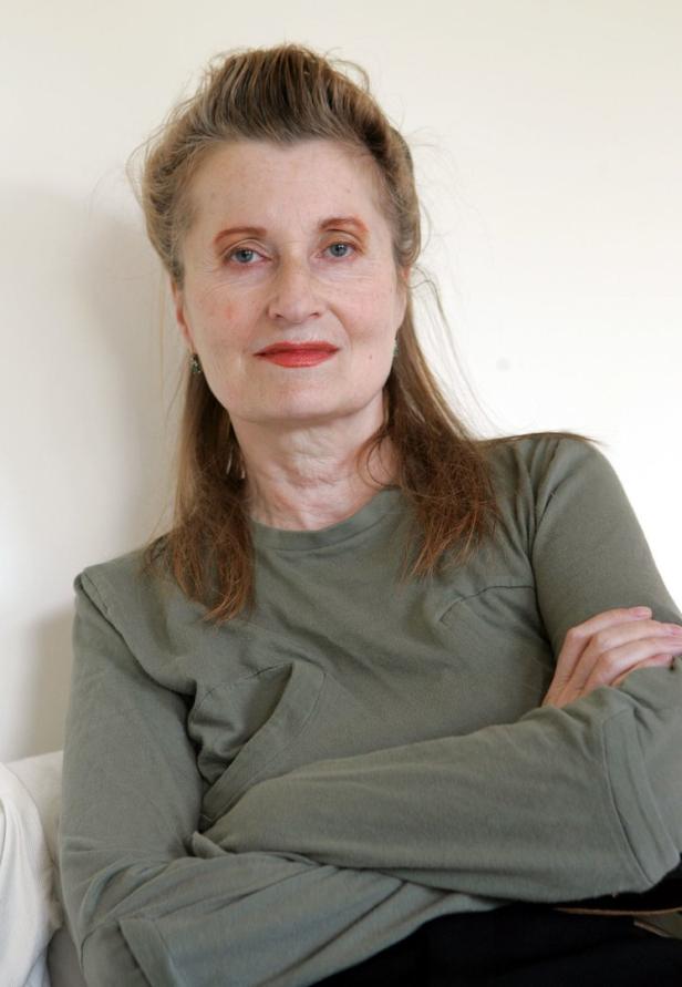 Eine Frau mit verschränkten Armen vor einem hellen Hintergrund.