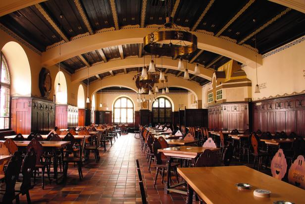 Ein großer Saal mit Holztischen und Stühlen, beleuchtet von Kronleuchtern.