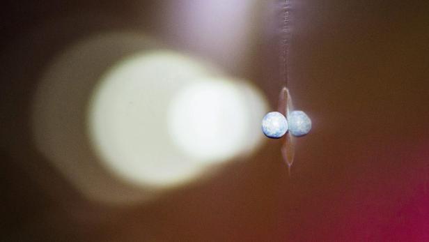 Zwei blaue Murmeln hängen an einem Faden vor einem verschwommenen Hintergrund.