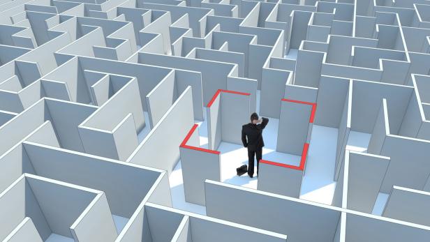 Ein Mann im Anzug steht in einem Labyrinth und kratzt sich am Kopf.