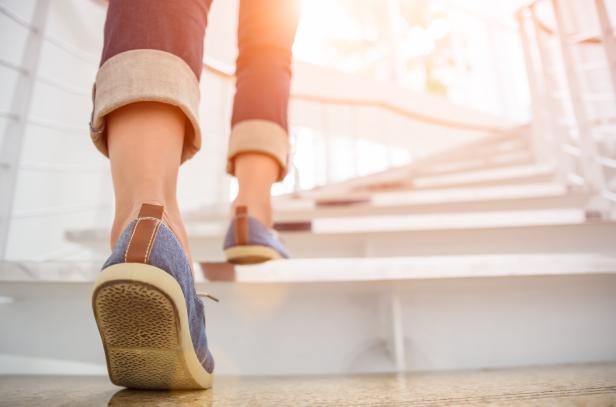 Eine Person in Jeans und blauen Schuhen steigt eine Treppe hinauf.