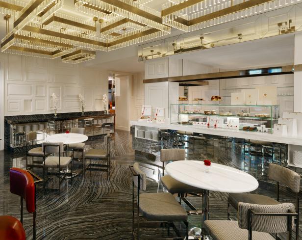 Innenansicht eines eleganten Cafés mit Tischen, Stühlen und einer Theke mit Gebäckauslage.