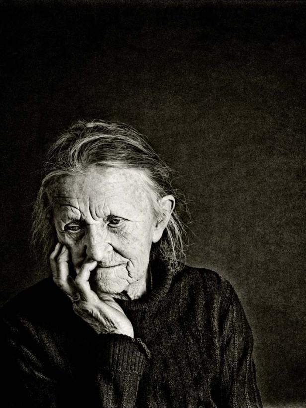 Eine ältere Frau mit müdem Blick stützt ihr Gesicht in die Hand.