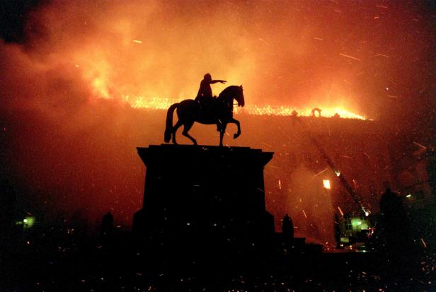 Eine Silhouette eines Reiterstandbilds vor einem orangefarbenen Himmel mit Feuerwerk.