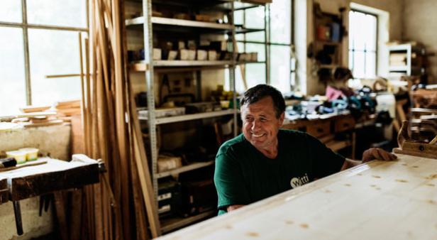 Ein lächelnder Tischler in seiner Werkstatt betrachtet eine Holzplatte.