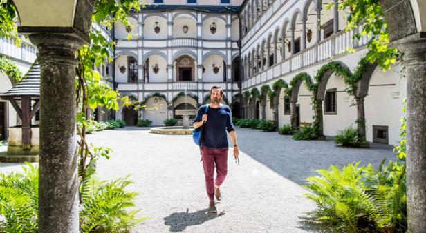 Ein Mann mit Rucksack geht durch den Innenhof eines Schlosses.