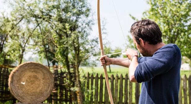 Ein Mann zielt mit Pfeil und Bogen auf eine Strohscheibe.