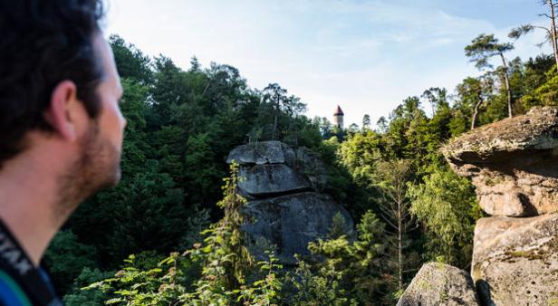 Ein Mann blickt auf eine Felsformation und einen Turm im Wald.