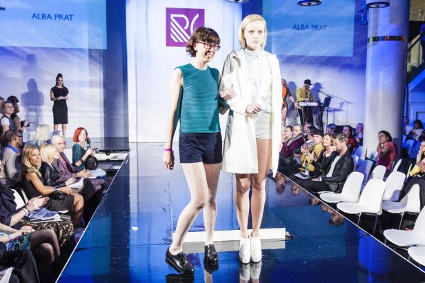 Zwei Frauen präsentieren Mode auf einem Laufsteg vor Publikum.