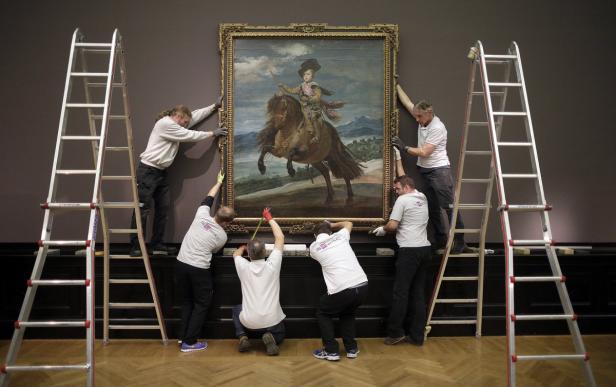 Mehrere Personen hängen ein großes Gemälde von einem Jungen auf einem Pferd in einem Museum auf.