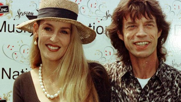 Jerry Hall und Mick Jagger posieren zusammen vor einer Sponsorenwand.