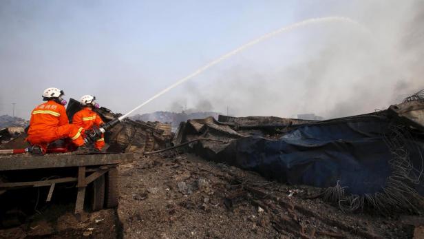 Zwei Feuerwehrleute löschen einen Brand in einem Trümmerfeld.