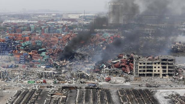 Eine zerstörte Lagerhalle mit Trümmern, Containern und ausgebrannten Autos nach einer Explosion.