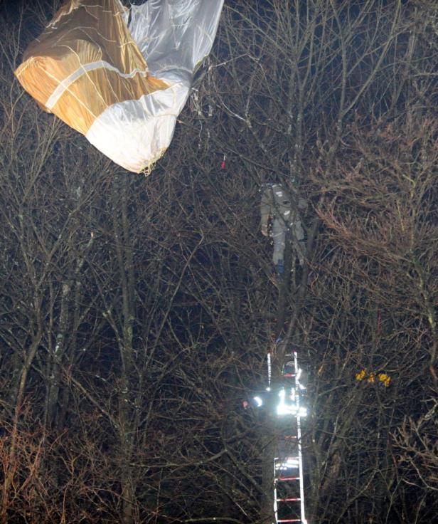 Ein Fallschirm hat sich in den Ästen eines Baumes verfangen; Rettungskräfte sind mit einer Leiter vor Ort.