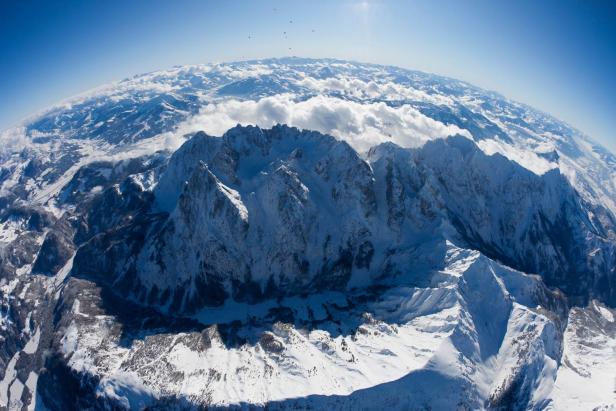 Eine Luftaufnahme einer schneebedeckten Bergkette unter blauem Himmel.
