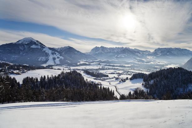 Winterliche Landschaft mit schneebedeckten Bergen und bewaldeten Hügeln.