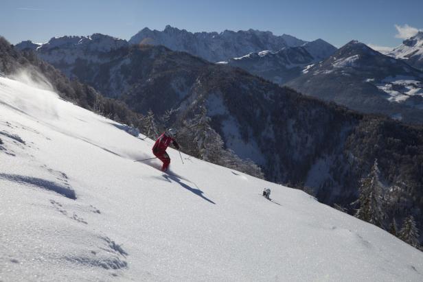 Ein Skifahrer fährt einen verschneiten Hang hinunter, im Hintergrund sind Berge zu sehen.