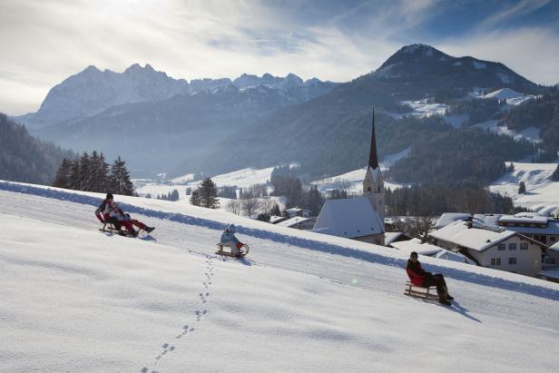 Winterlandschaft mit Menschen, die auf einer schneebedeckten Piste rodeln.