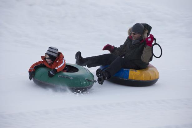 Ein Kind und ein Erwachsener fahren auf Luftreifen einen schneebedeckten Hügel hinunter.