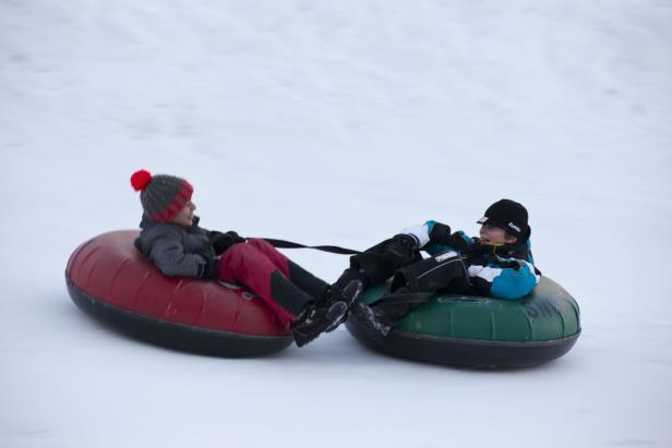 Zwei Kinder fahren auf Reifen einen schneebedeckten Hügel hinunter.