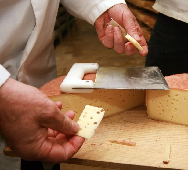 Ein Käse wird mit einem Käsehobel in Scheiben geschnitten.