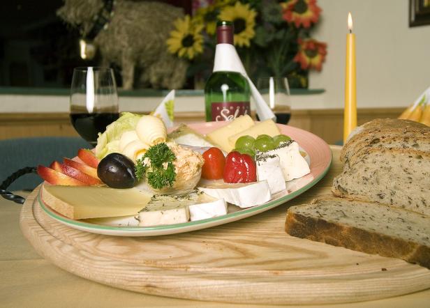 Ein Käseteller mit Brot, Obst und einer Flasche Wein auf einem Tisch.