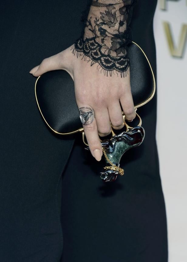 Eine Hand mit Spitzenärmel hält eine schwarze Clutch mit auffälligem Schmuck.