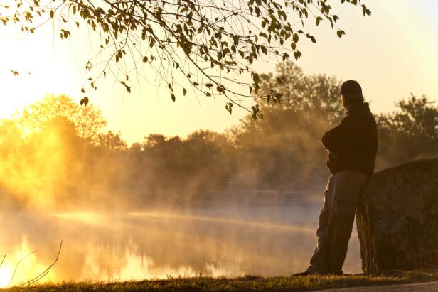 Adult Male Stands Alone At Sunrise Staring Towards Foggy Lake