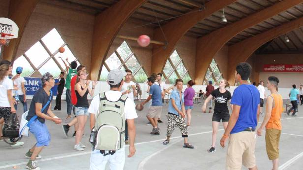 Eine Gruppe junger Leute spielt Basketball in einer Halle.