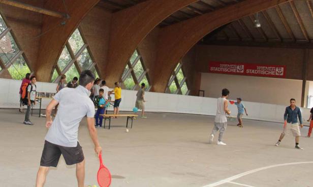 Eine Gruppe von Menschen spielt Ball unter dem Dach einer Halle.