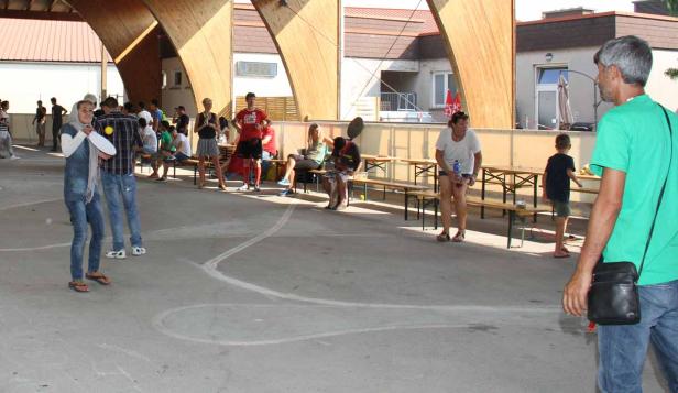 Eine Gruppe von Menschen versammelt sich unter einer Holzkonstruktion, einige spielen Frisbee.