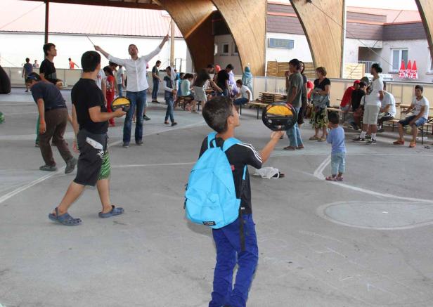 Eine Gruppe von Menschen versammelt sich unter einem offenen Holzdach, einige spielen mit Tellern.