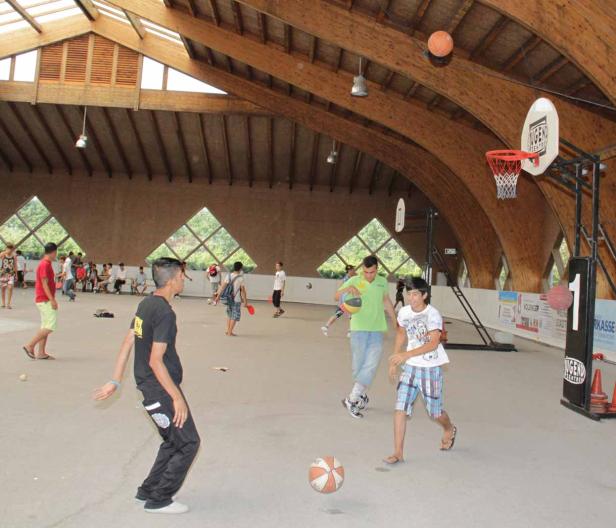 In einer Halle spielen Jugendliche Basketball und andere Spiele.