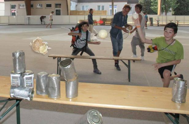 Eine Gruppe von Jugendlichen spielt mit Dosen und Bällen auf einem Schulhof.