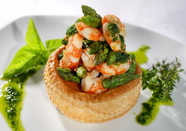 Ein Blätterteiggebäck gefüllt mit Spargel und Garnelen, garniert mit Kräutern und Pesto.