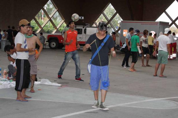 Eine Gruppe junger Leute verbringt Zeit in einer Halle, einer jongliert mit einem Diabolo, ein anderer balanciert einen Ball auf dem Kopf.