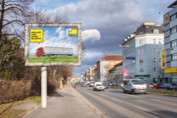 Eine Werbetafel mit einem LKW steht an einer Straße in der Stadt.