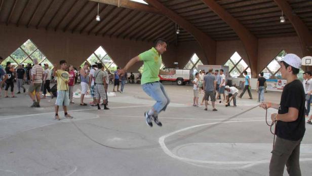 Ein Mann springt über ein langes Seil, das von zwei Personen gehalten wird.