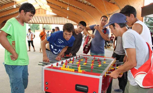 Eine Gruppe junger Männer spielt Tischfußball in einer Halle.