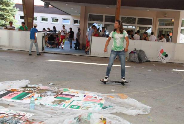 Eine junge Frau fährt auf einem Skateboard über einen Platz mit Farbresten.