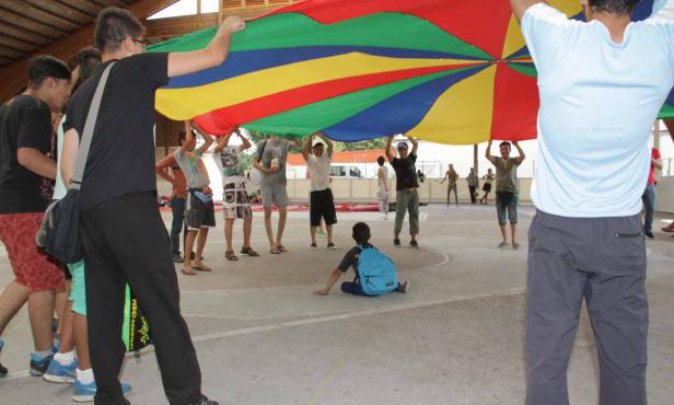 Eine Gruppe von Jugendlichen hält ein buntes Schwungtuch in einer Turnhalle hoch.