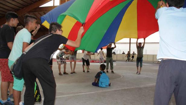 Eine Gruppe von Kindern spielt mit einem bunten Schwungtuch in einer Halle.