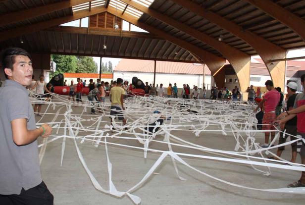 Eine Gruppe von Menschen spielt ein Spiel mit langen, weißen Papierstreifen in einer Halle.