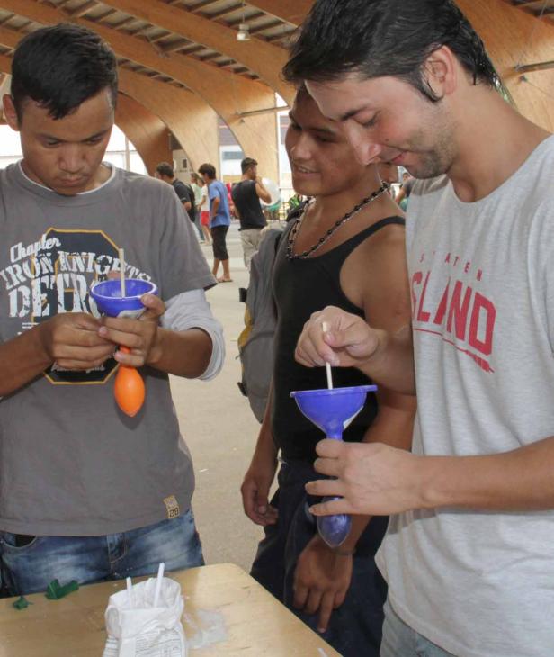 Drei junge Männer basteln mit Trichtern und Ballons an einem Tisch.