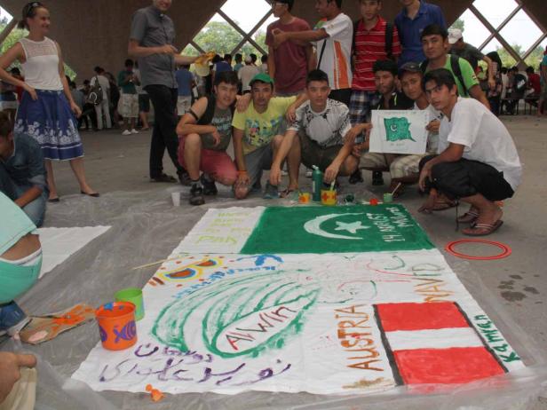 Eine Gruppe junger Leute malt eine große Flagge Pakistans und andere Motive auf ein Tuch.