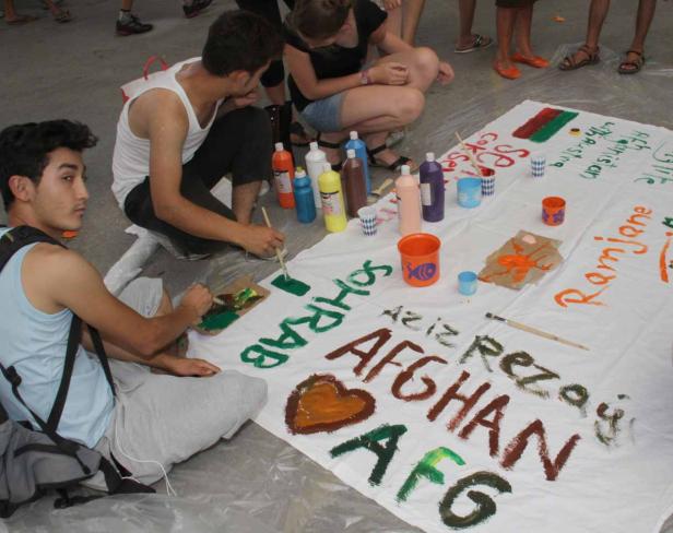 Mehrere Personen malen gemeinsam ein großes Transparent mit dem Schriftzug „AFGHAN AFG“.