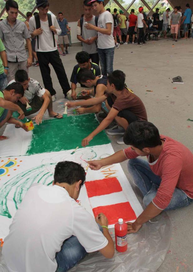 Eine Gruppe junger Männer malt gemeinsam auf einer großen Leinwand.