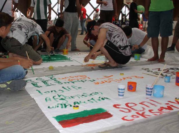 Eine Gruppe von Menschen malt gemeinsam ein großes Banner mit Friedensbotschaften.